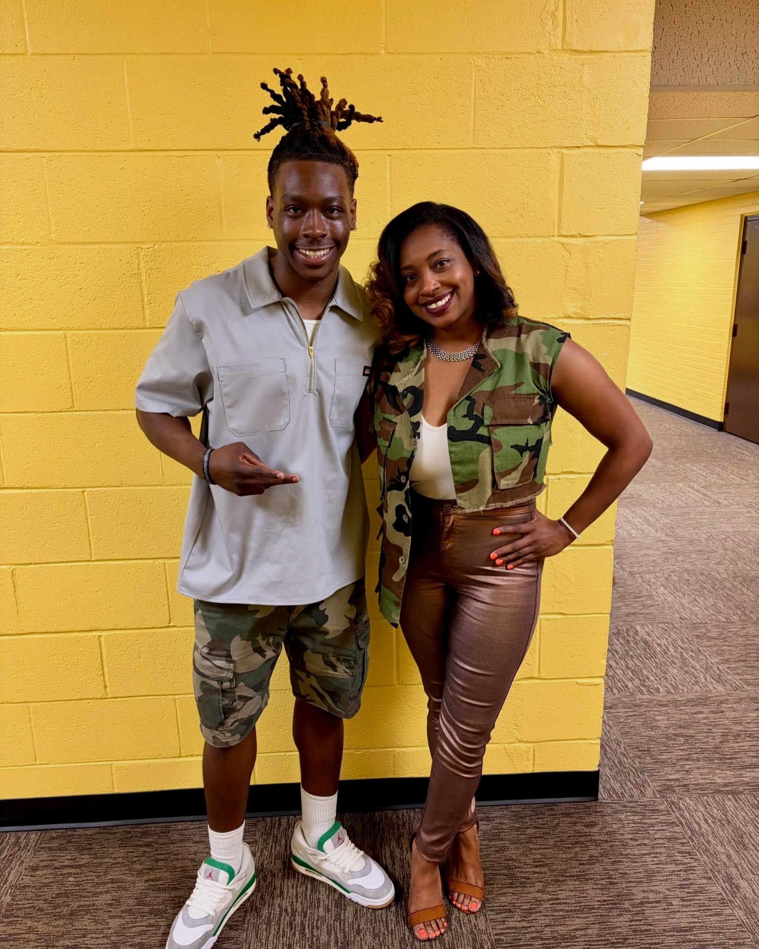 A young man and a leader posing together against a yellow wall after service.