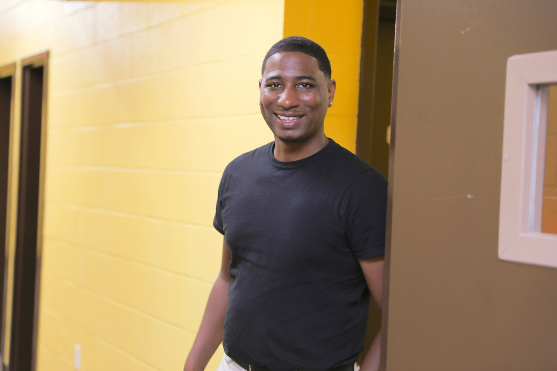 A young man in a black tee smiling in a bright church hallway.