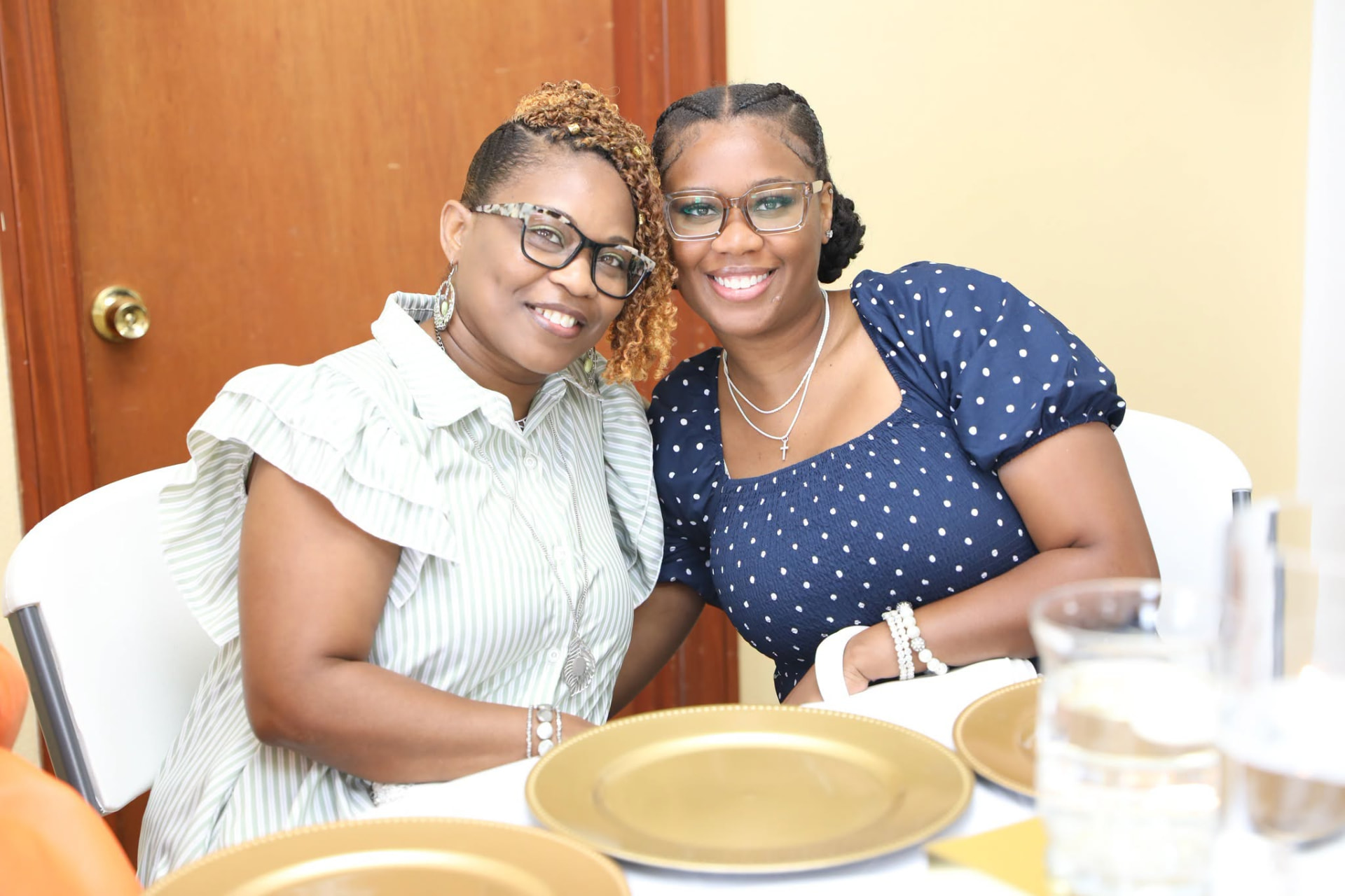 Two women smiling cheek to cheek at a banquet table set with gold chargers.
