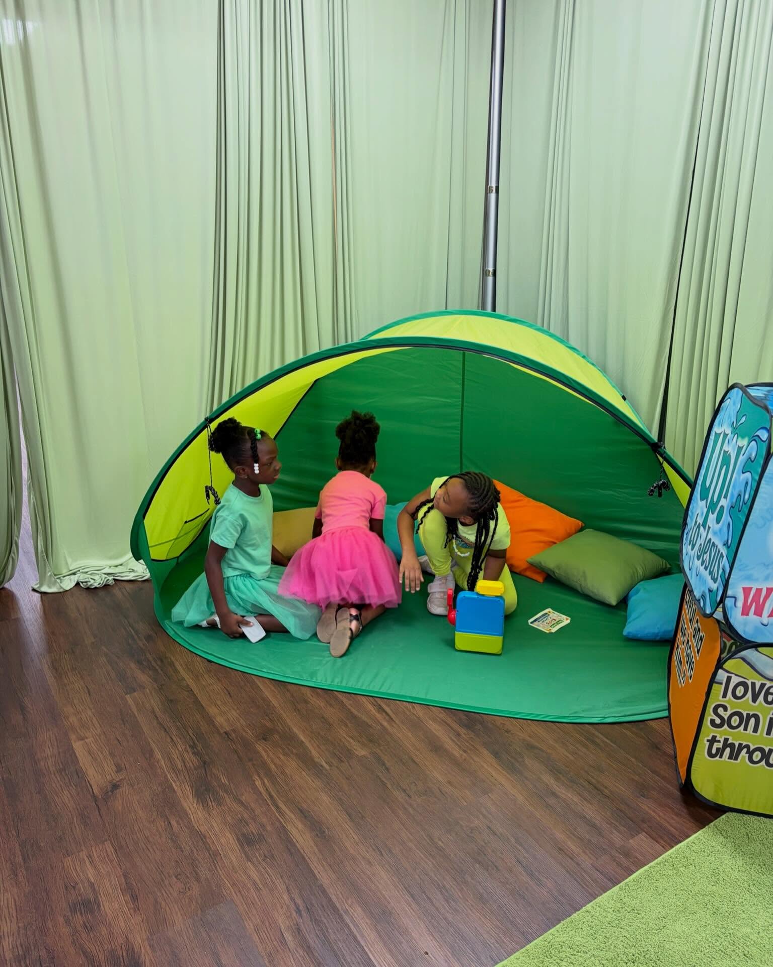Three girls playing inside a green tent in the children's ministry room.